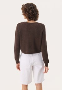 Brauner Rippstrickpullover mit langen Ärmeln, cropped Design, kombiniert mit weißen Denim-Shorts, Rückansicht zeigend und einer einfachen, klaren Textur.