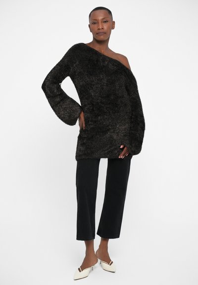 Must sheremüük oversized-sweater, üks õlg paljas. Kombineeritud mustade lühikeste teksade ja kreemjade terava ninaga muulidega.