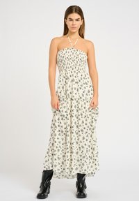 Rochie maxi de culoare albă-crem cu imprimeu floral negru, design fără bretele, cu bust din bumbac elastic și fustă fluidă. Asociată cu cizme negre până la gleznă.