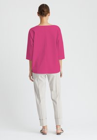 Fuchsia Oversized-Oberteil mit drei Viertelärmeln, Rundhalsausschnitt und Rückennaht, kombiniert mit hellbeigen, tapered Hosen und Sandalen.