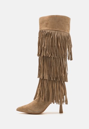 Hochhackiger kniehoher Stiefel aus Wildleder in Tan mit mehrlagigem Fransenbesatz, verziert mit kleinen silbernen Nieten, vor schlicht weißem Hintergrund.