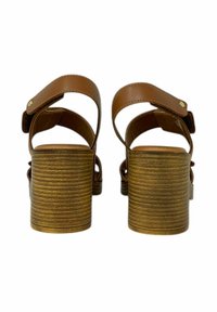 Sandali con tacco alto marroni, con un tacco in legno texturizzato, cinturino alla caviglia regolabile e parte superiore in pelle liscia. La vista posteriore mostra la posizione del cinturino.