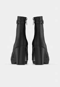 Botas pretas até ao tornozelo com acabamento em pele lisa, design afunilado e um salto grosso. Inclui um fivela ajustável e um fecho em zíper na parte de trás.