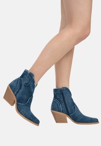 Botas de tobillo de denim con acabado texturizado, cremallera lateral y tacón apilado. Presentan bordes deshilachados y un diseño de punta afilada.