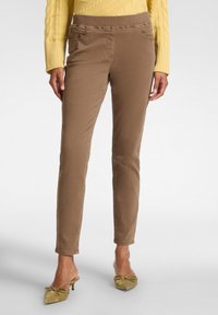 Pantalones marrones de corte slim con una textura suave, que cuentan con bolsillos laterales y una cinturilla elástica, combinados con zapatos verdes adornados con un lazo.