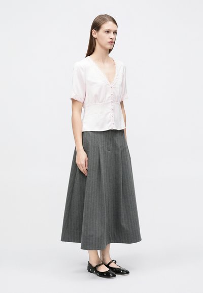 Ροζ μπλούζα με κοντά μανίκια, διακοσμημένη με δαντέλα και κουμπιά· συνοδεύεται από γκρι, μακρύ μέχρι το έδαφος, πλισέ φούστα· μαύρα επίπεδα παπούτσια.