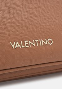 Ruskea teksturoitu nahkakassi, jossa on tyylikäs muotoilu ja voimakas kultainen "VALENTINO" -logo.