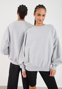 Felpa oversize di un grigio chiaro con maniche lunghe e svasate e scollatura rotonda. Polsini e orlo a coste. Tessuto morbido e vestibilità rilassata.