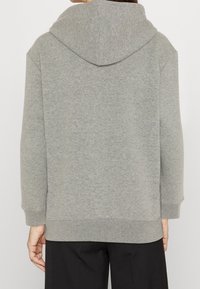 Sudadera gris hecha de una tela suave, con una capucha grande, mangas largas y un ajuste relajado. Sin patrones visibles ni detalles de hardware.