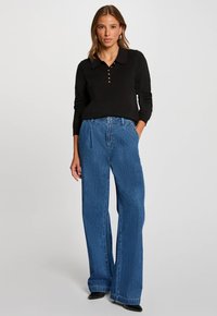 Maglione nero a maniche lunghe con colletto e dettagli di bottoni, abbinato a jeans blu a vita alta e gamba larga. Texture liscia, vestibilità casual.
