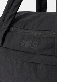 Czarna torba na ramię z teksturowanej tkaniny, centralną kieszenią na zamek oraz metką z logo "ROSIE" i małą grafiką. Wytrzymałe uchwyty.