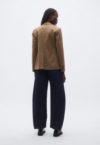 Brun skræddersyet blazer med struktureret design og hakskraver, kombineret med mørke vide jeans. Glat stof og minimalistiske detaljer.