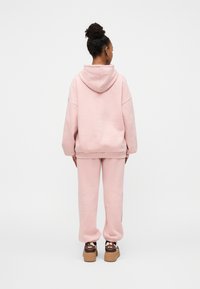 Sweat à capuche oversize rose à cordon, accompagné d'un pantalon de jogging assorti. Le tissu est doux, avec des poignets côtelés et une coupe décontractée.