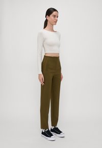 White long-sleeve crop top paired with olive high-waisted pants featuring side pockets and a straight cut, worn with navy sneakers.
