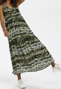 Maxi-jurk in groen en zwart abstract patroon, mouwloos met een V-hals, vloeiende stof, gelaagd ontwerp, gecombineerd met witte sneakers.