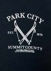 Mornarska bombažna majica z belim tiskanim besedilom in čez križ postavljenimi ilustracijami smuči. Besedilo vključuje "Park City," "Summit County," in leto ustanovitve "1975."