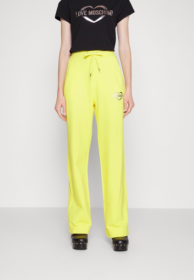 Gula joggingsbyxor med dragsko i midjan och logotyp, i kombination med en svart T-shirt med metallisk text. Slät tyg, lös passform.