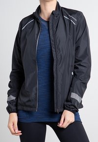 Chaqueta cortavientos negra ligera con acentos reflectantes y un alto cuello. Cuenta con puños elásticos y una cremallera frontal completa.