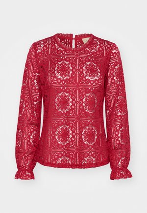 Piros csipkés, hosszú ujjú blúz, amely bonyolult virágmintákkal, kerek nyakkivágással és fodros mandzsettákkal rendelkezik. Kulcsszerű hátkivágás.