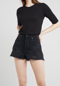 Camiseta de algodón negra con manga corta combinada con pantalones cortos de mezclilla negra que presentan detalles desgastados, dobladillos deshilachados y un diseño de talle alto.