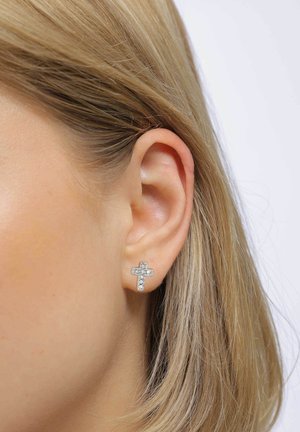 Øreringe i sølvtonet kors med klare rhinstenaccent, med en struktureret finish og en stiftedesign, placeret mod en lys baggrund.