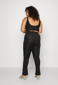 Top corto a coste nero e leggings neri a vita alta, con una texture liscia. Il modello indossa sandali con tacco verde menta.