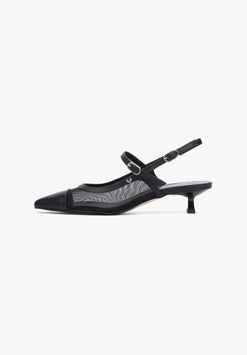 Zapato negro de tacón bajo con punta afilada, que presenta una parte superior de malla transparente, acentos de cuero y un tacón tipo kitten. Detalle en hardware dorado visible.