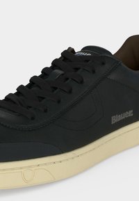Baskets en cuir noir avec lacets noirs, semelle beige et logo "Blauer" sur le côté, vues en gros plan sous un angle.