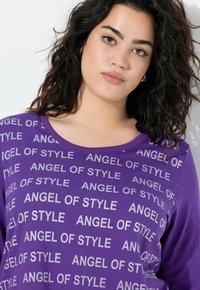 Maglietta a maniche lunghe di colore viola con testo metallico argento "ANGEL OF STYLE" ripetuto sul davanti, caratterizzata da un colletto rotondo e una texture di tessuto morbido.