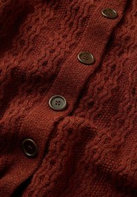 Rostfärgad stickad cardigan med ett strukturerat kabelmönster, som har mörkbruna knappar och ett mjukt, varmt tyg.