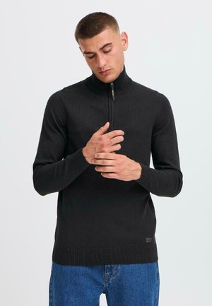 Pull noir à manches longues avec un col haut et un zip demi-longue à l'avant. Poignets côtelés et ourlet. Fabriqué en tissu tricoté lisse, avec un détail de marque minimal.