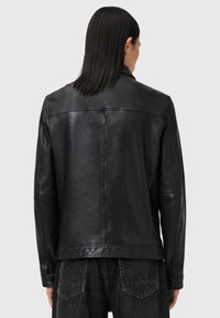 Veste en cuir noir avec une texture lisse, un design ajusté et des détails de couture minimalistes. Présente un col classique et un dos ouvert.