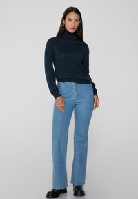 Suéter de cuello alto azul marino combinado con jeans rectos de color azul claro, que presentan una textura sutil y botas negras de tobillo con suela rugged.