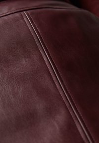 Burgundy lädermaterial med en slät textur, med två parallella sömmar för detalj. Fokus på mjukt utförande och färgdjup.
