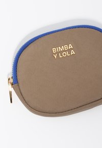 Pruun kangaskott sinise tõmblukuga ja kuldse riistvaraga, mille esiküljel on reljeefselt printitud tekst "BIMBA Y LOLA".