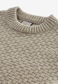Beige knitted sweater with a textured, woven pattern. Features a ribbed crew neckline and a label sewn inside the collar.