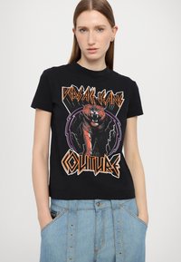 Μαύρο βαμβακερό μπλουζάκι με γραφικό μοτίβο τίγρης με πορτοκαλί και μωβ λεπτομέρειες. Έχει κοντά μανίκια και στρογγυλή λαιμόκοψη, φορεμένο με ανοιχτόχρωμο τζιν παντελόνι.