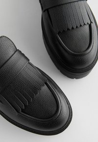 Black leather shoes featuring a textured surface, a flat sole, and fringed accents on the upper design and vamp.