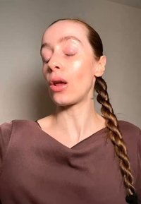 Kvinne med langt flettet hår, iført en brun topp, øynene lukket, munnen lett åpen, mot en ensfarget lys bakgrunn.