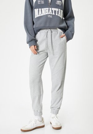 Pantaloni grigi in felpa realizzati con tessuto morbido, dotati di vita elastica, gambe affusolate e orli a costina. Indossati con una felpa blu e sneaker bianche.