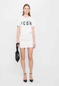 Robe T-shirt en coton blanc avec "ICON" imprimé en noir gras, associée à un sac à main noir et des chaussures à talons hauts noires. Texture lisse.