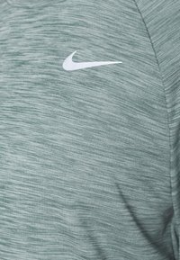 Nike Sport-T-Shirt in hellem Grün, aus einem feinen, strukturierten Stoff mit einem dezenten Melange-Muster und einem weißen Logo auf der Brust.