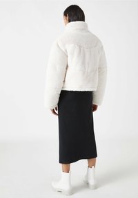 Chaqueta de forro polar blanca con cuello alto y corte cuadrado, combinada con una falda negra de canalé y botines blancos con cordones.