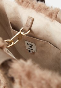 Beige suede tas interieur met zachte, pluizige textuur, gouden hardware en een label met 'BOSS' en 'Steiff' merken.