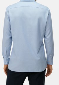 Světle modrá košile s dlouhým rukávem, hladkou strukturou, manžetami na knoflíky a špičatým límcem. Pohled zezadu ukazuje přiléhavý střih a ploché sedlo.
