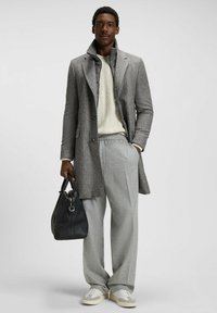 Grå mönstrad överrock, vit kabelstickad tröja, grå byxor, svart handväska och ljusa sneakers. Har en skräddarsydd passform och en strukturerad design.