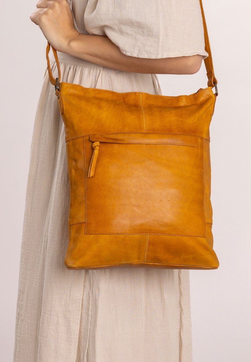 Gul lädercrossbody-väska med platt design, med en dragkedjeficka på framsidan och en axelrem. Slät textur.