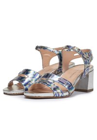 Avoin varvas sandaalit, joissa on iridesoivaa kangasta, hopeiset metalliset yksityiskohdat ja paksu korko. Ominaisuuksia ovat ristiin menevät remmit ja säädettävä nilkkahihna.