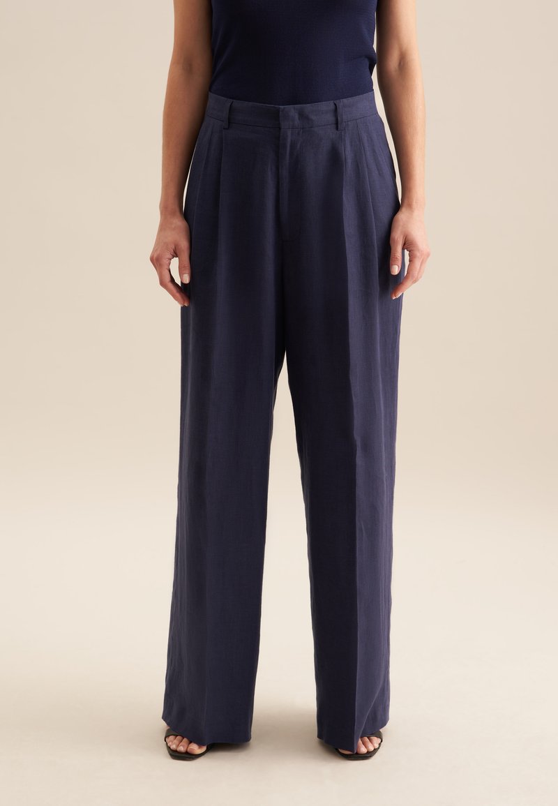 Pantalon large navy en lin. Il présente une taille haute avec des plis et une texture lisse, conçu pour un ajustement décontracté.