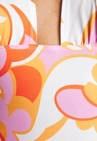 Tecido de fato de banho com um padrão floral vibrante em laranja, rosa e branco. Apresenta um decote em forma de scoop e costuras visíveis ao longo das bordas.